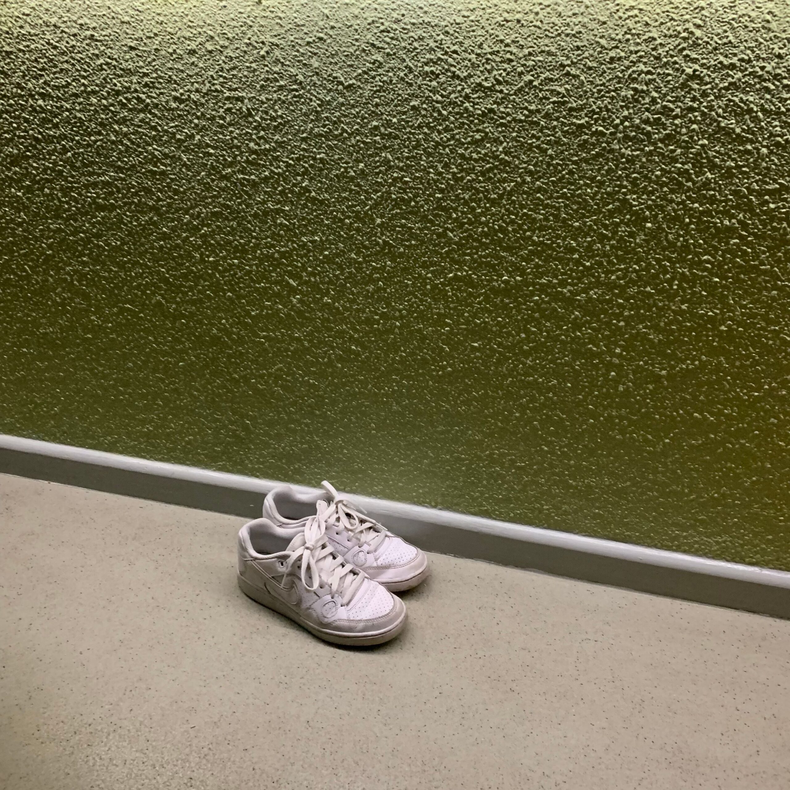 Clean white leather court sneakers against an olive green wall