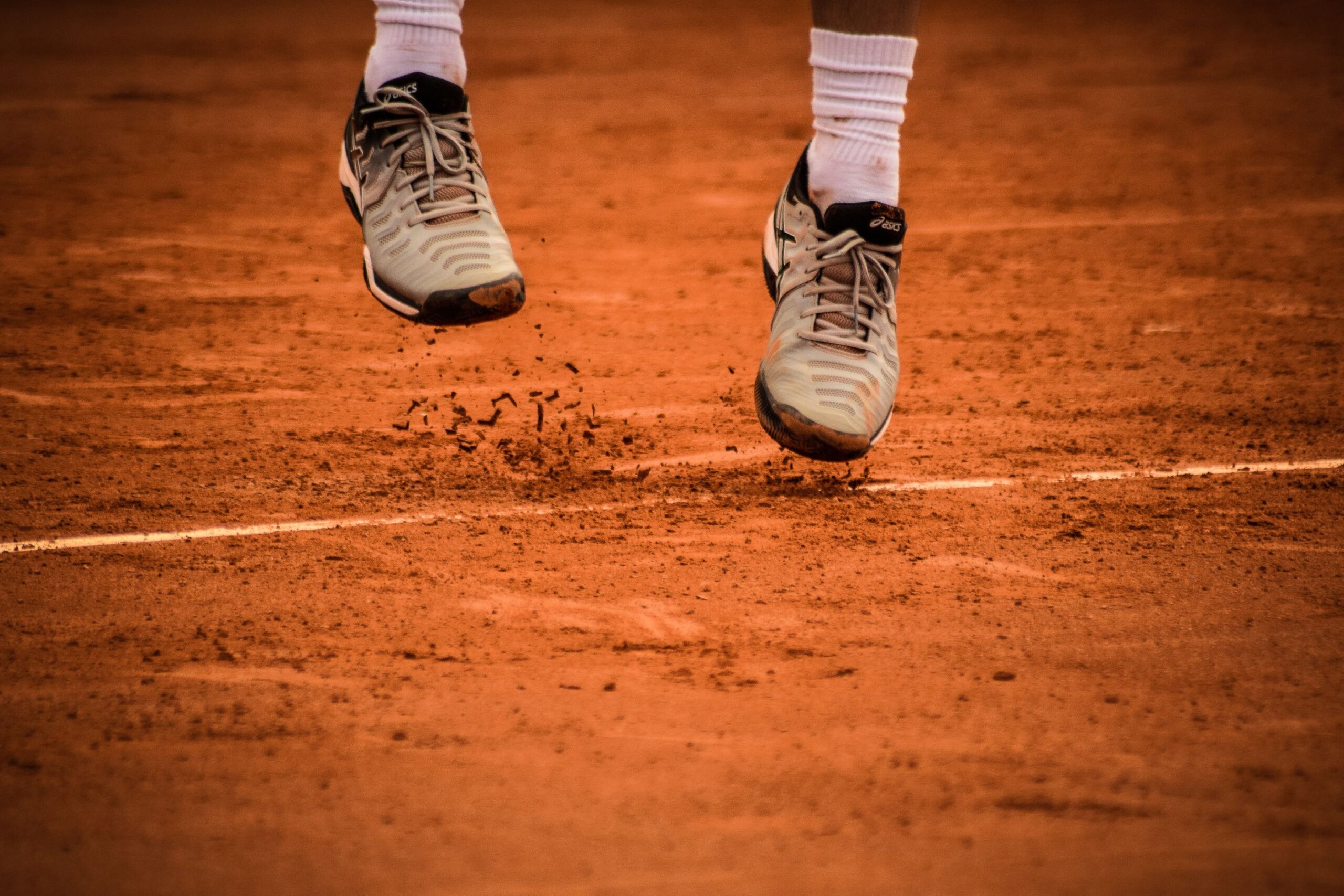 Close-up of court shoes mid-movement, kicking up clay on a tennis court