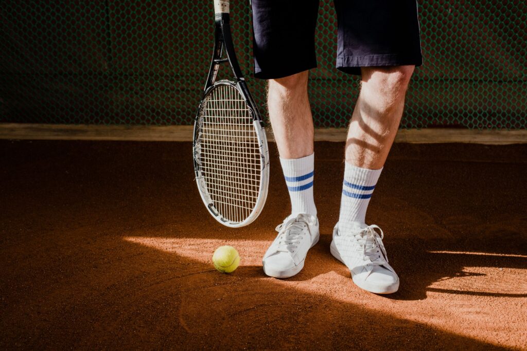 Tennis player on a clay court with a racquet, a ball, and white court sneakers