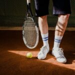 Tennis player on a clay court with a racquet, a ball, and white court sneakers