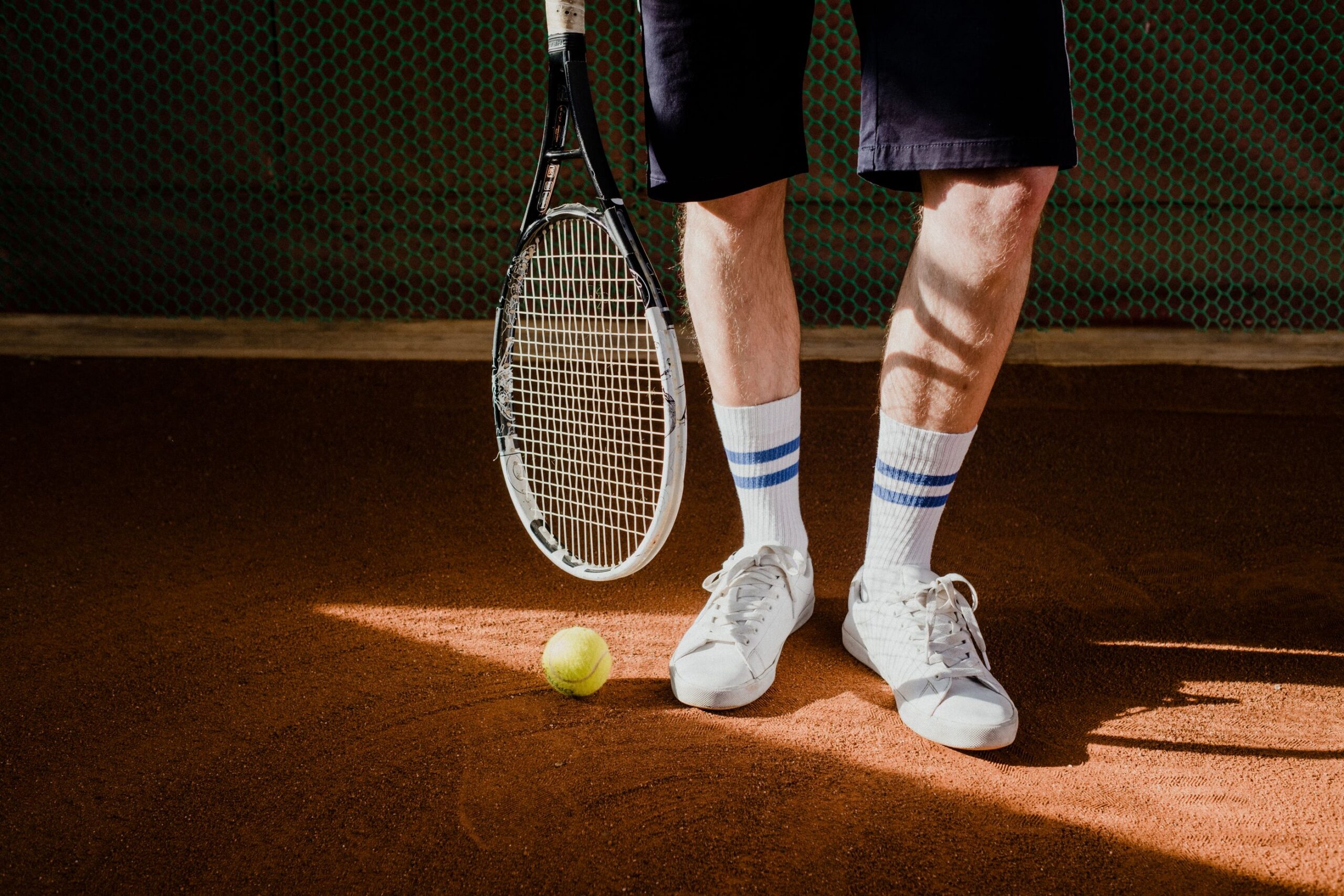 Tennis player on a clay court with a racquet, a ball, and white court sneakers